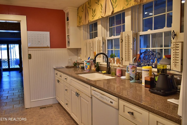 kitchen featuring sink, dishwasher, white cabinetry, and dark stone counters