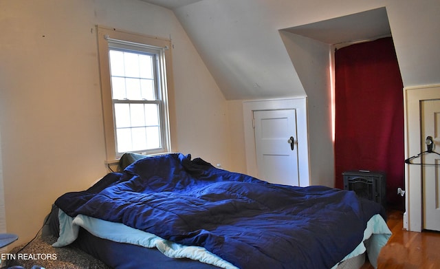 bedroom with hardwood / wood-style flooring, a wood stove, and vaulted ceiling