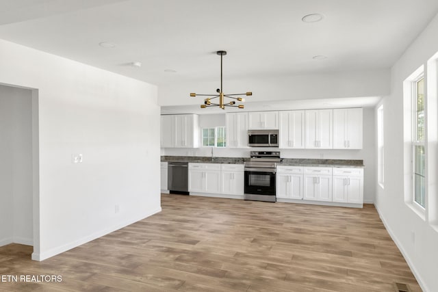 kitchen featuring hanging light fixtures, light wood-type flooring, stainless steel appliances, white cabinets, and a chandelier