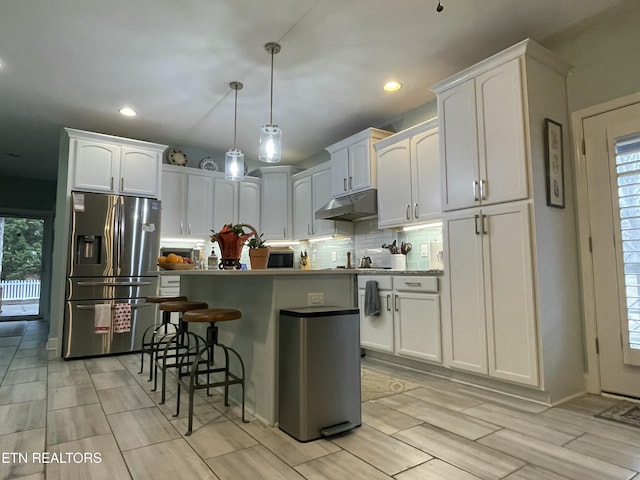 kitchen with white cabinets, a center island, tasteful backsplash, hanging light fixtures, and stainless steel fridge