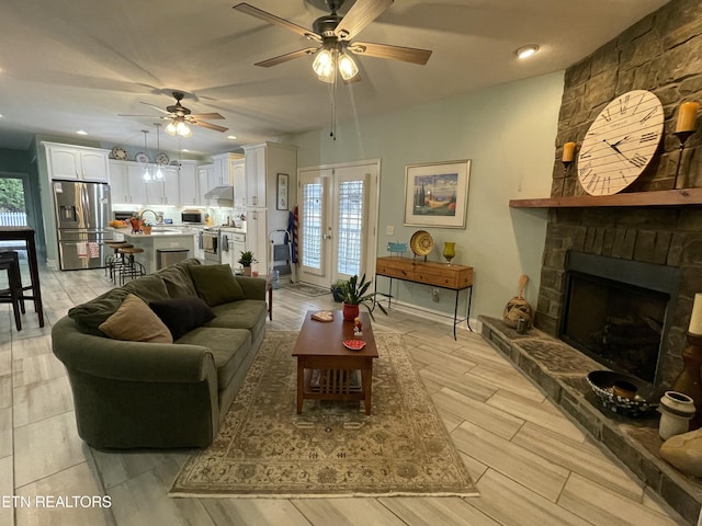 living room featuring ceiling fan, french doors, a fireplace, and sink