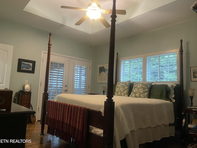 bedroom with hardwood / wood-style floors, ceiling fan, access to outside, a tray ceiling, and french doors