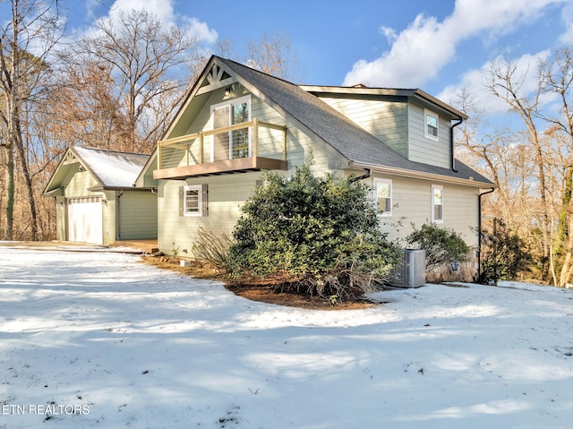 view of snowy exterior featuring a garage, central air condition unit, and a balcony