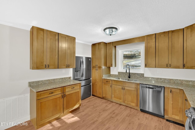 kitchen featuring appliances with stainless steel finishes, light stone countertops, a textured ceiling, light hardwood / wood-style flooring, and sink