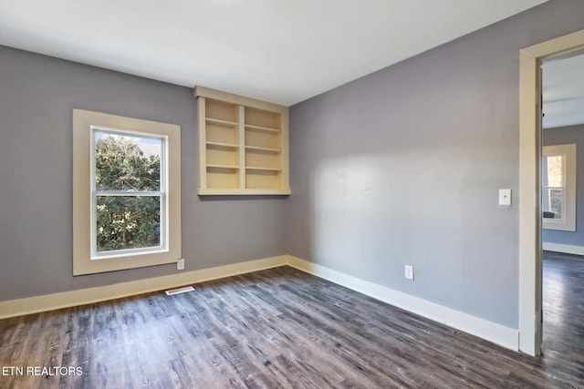 empty room featuring dark hardwood / wood-style floors and built in shelves