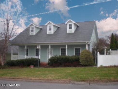 cape cod-style house featuring covered porch, fence, and a front lawn