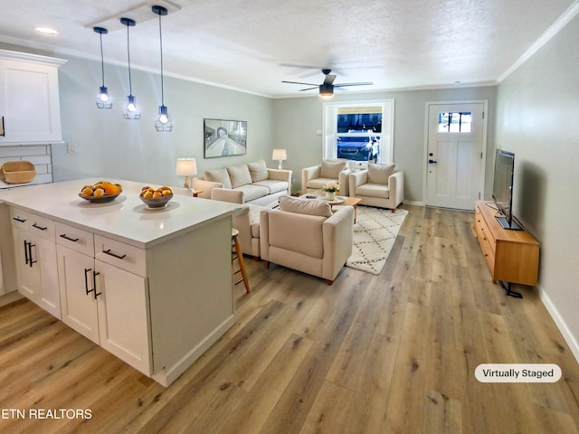 living room with ornamental molding, ceiling fan, a textured ceiling, and light hardwood / wood-style flooring