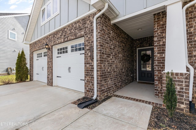 doorway to property with a garage, driveway, brick siding, and board and batten siding