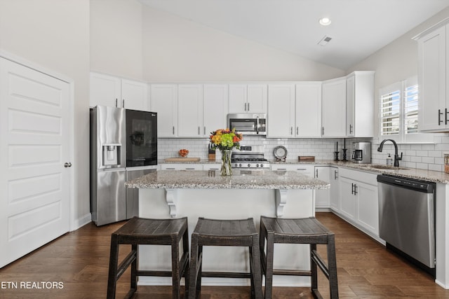 kitchen featuring stainless steel appliances, a kitchen island, white cabinets, and light stone countertops