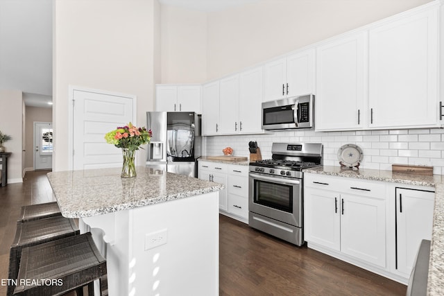 kitchen with white cabinets, light stone countertops, stainless steel appliances, and a center island