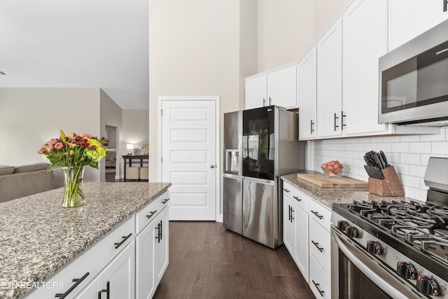 kitchen featuring dark wood finished floors, stainless steel appliances, backsplash, white cabinetry, and light stone countertops