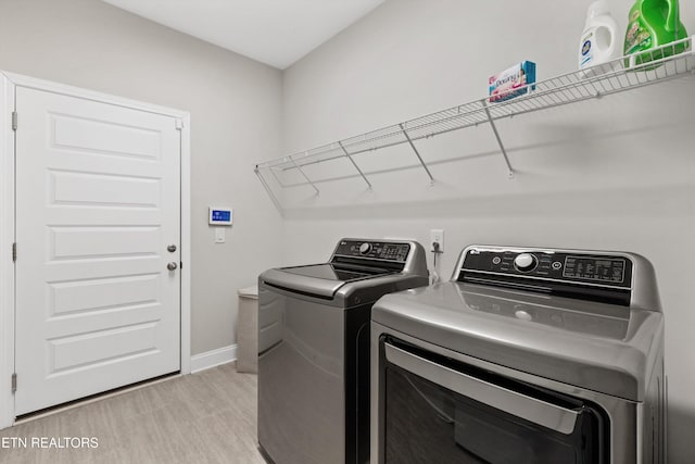 clothes washing area with laundry area, baseboards, light wood finished floors, and washing machine and clothes dryer