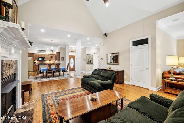 living room with light wood-type flooring, ceiling fan with notable chandelier, high vaulted ceiling, and ornamental molding