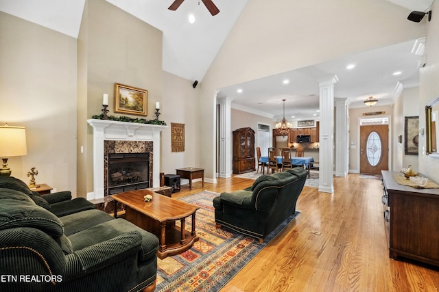 living room with a high end fireplace, ornate columns, light hardwood / wood-style floors, ornamental molding, and ceiling fan