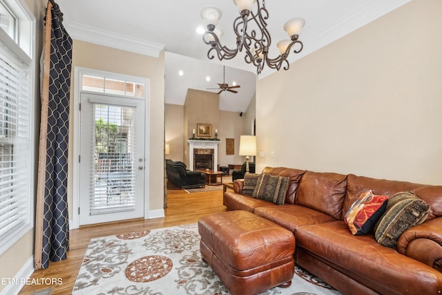 living room with crown molding, a large fireplace, light hardwood / wood-style flooring, ceiling fan with notable chandelier, and lofted ceiling