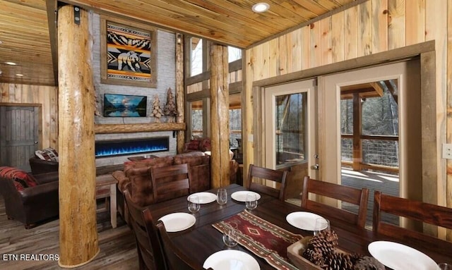 dining area with wood ceiling, dark hardwood / wood-style flooring, wooden walls, and a stone fireplace