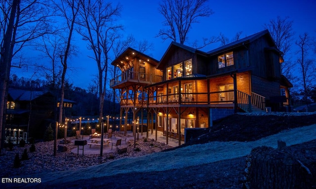 back house at twilight featuring a balcony, a patio area, and a fire pit