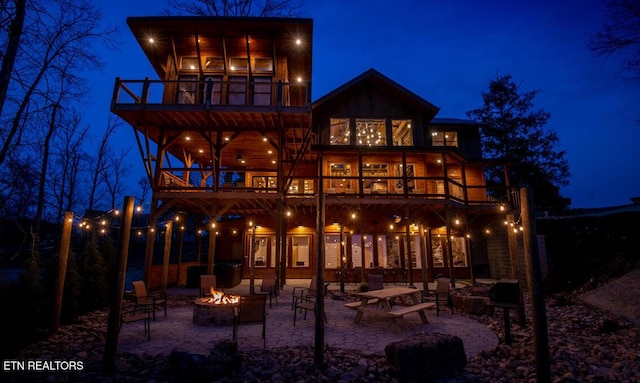 back house at twilight featuring a patio area, a balcony, and a fire pit