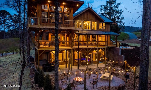 back house at dusk featuring a balcony, a patio area, and a fire pit