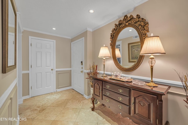 foyer entrance with ornamental molding, a wainscoted wall, visible vents, and light tile patterned floors