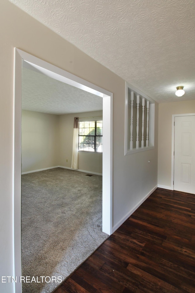 empty room with visible vents, dark wood finished floors, a textured ceiling, and baseboards