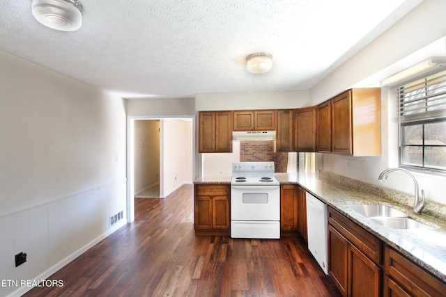 kitchen with light stone countertops, under cabinet range hood, white appliances, a sink, and brown cabinets