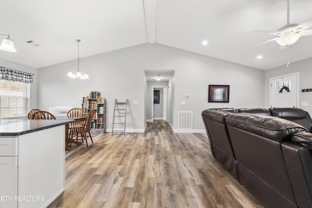 living room featuring light wood-type flooring, lofted ceiling, and ceiling fan with notable chandelier