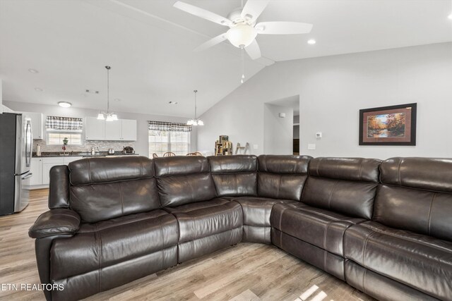 living room featuring ceiling fan with notable chandelier, light hardwood / wood-style flooring, and lofted ceiling