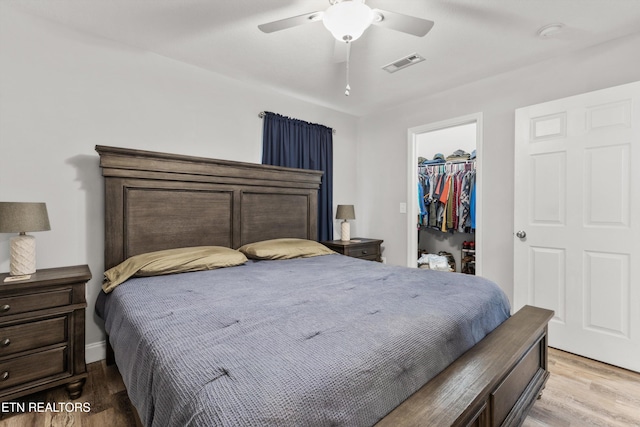 bedroom featuring ceiling fan, a closet, light hardwood / wood-style flooring, and a walk in closet