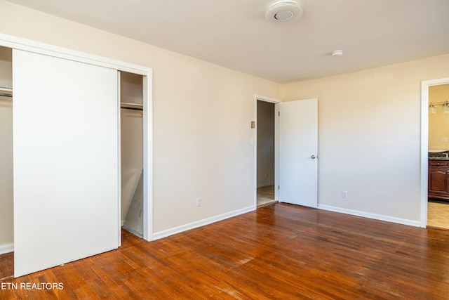 unfurnished bedroom with dark wood-type flooring, ensuite bathroom, and a closet