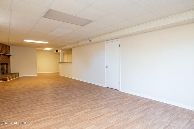 basement with light hardwood / wood-style floors, a paneled ceiling, and a brick fireplace