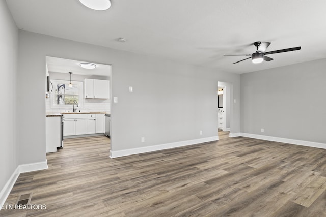 unfurnished living room featuring a ceiling fan, a sink, baseboards, and wood finished floors