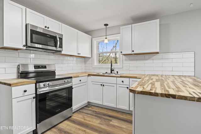 kitchen with dark wood-style flooring, wooden counters, appliances with stainless steel finishes, a sink, and a peninsula