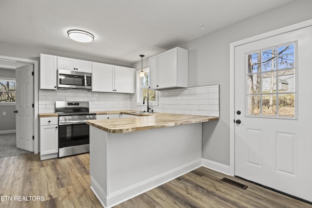 kitchen with a peninsula, butcher block countertops, a sink, visible vents, and appliances with stainless steel finishes