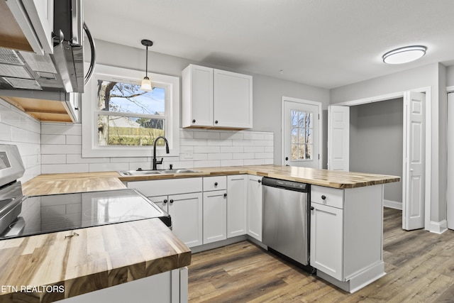 kitchen featuring stainless steel appliances, a sink, wood counters, and a peninsula