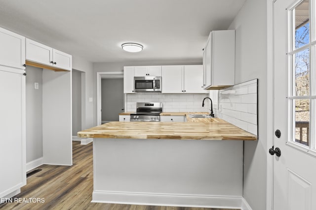 kitchen with wooden counters, decorative backsplash, appliances with stainless steel finishes, a sink, and a peninsula