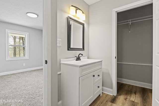 bathroom with wood finished floors, a walk in closet, vanity, and baseboards