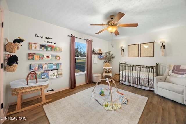 bedroom featuring dark wood-type flooring, ceiling fan, a textured ceiling, and a nursery area