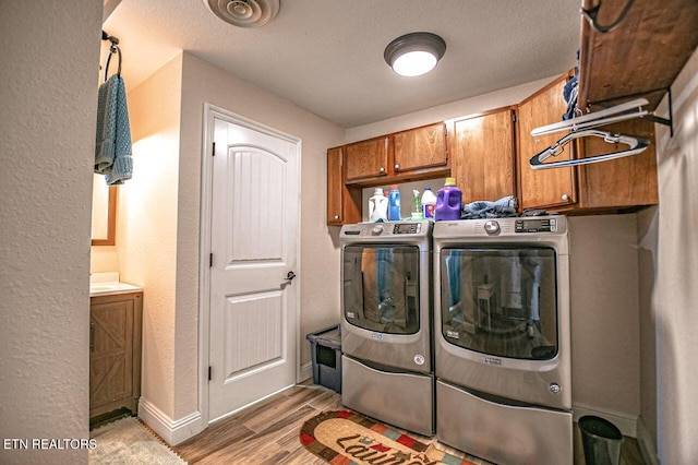 laundry room with cabinets, a textured ceiling, washing machine and clothes dryer, and light hardwood / wood-style floors