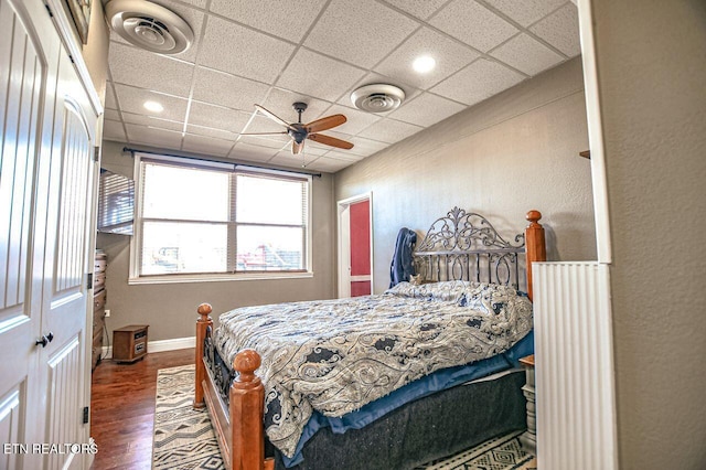 bedroom with dark wood-type flooring, a paneled ceiling, ceiling fan, and a closet