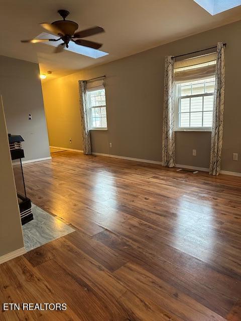 unfurnished room with ceiling fan, a skylight, and dark hardwood / wood-style flooring