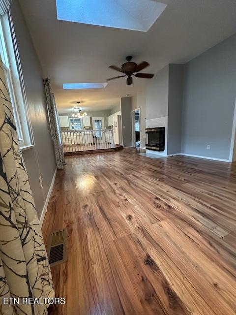 unfurnished living room with ceiling fan with notable chandelier, wood-type flooring, and a skylight