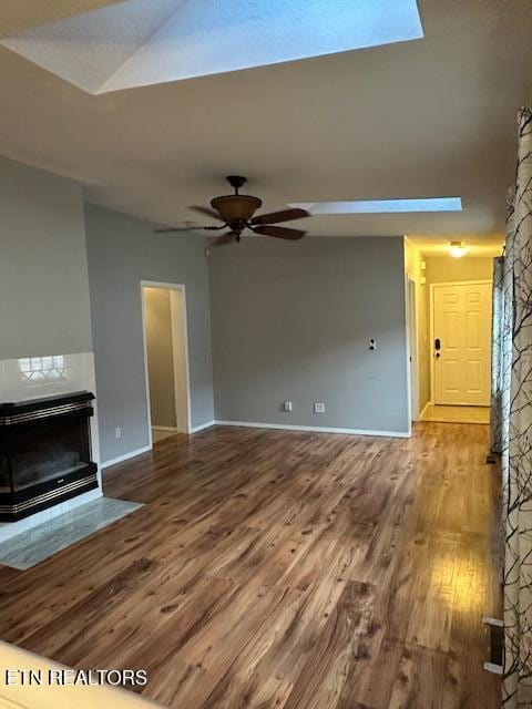 unfurnished living room featuring ceiling fan, wood-type flooring, and a stone fireplace