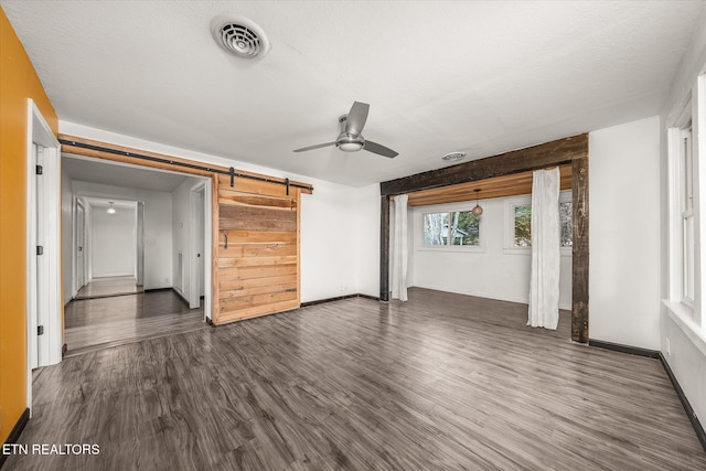 unfurnished living room with a textured ceiling, dark wood-type flooring, a barn door, and ceiling fan