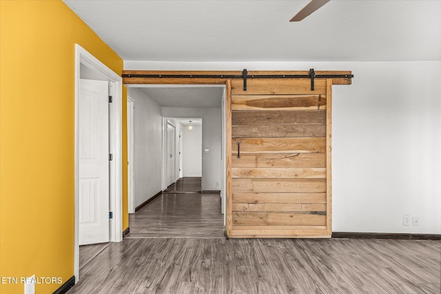 spare room with a barn door, ceiling fan, dark hardwood / wood-style floors, and a textured ceiling