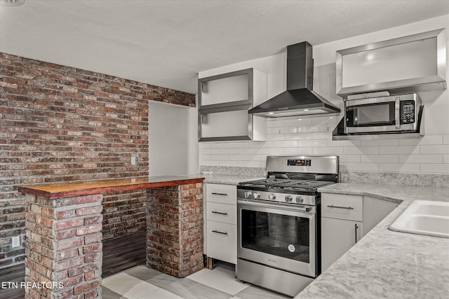 kitchen featuring wall chimney exhaust hood, sink, a textured ceiling, stainless steel appliances, and backsplash