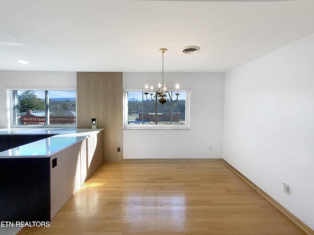 unfurnished dining area featuring a notable chandelier and light hardwood / wood-style floors