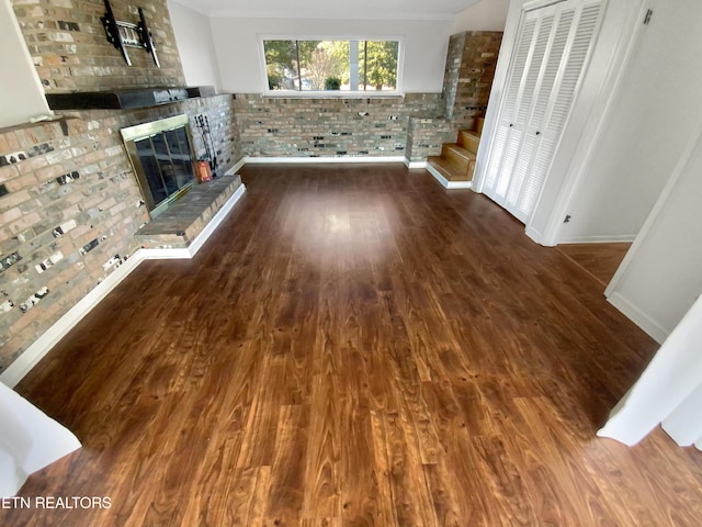 unfurnished living room with hardwood / wood-style floors, brick wall, and a brick fireplace