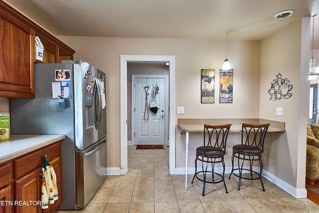 kitchen featuring decorative light fixtures, light tile patterned floors, stainless steel fridge, and a breakfast bar