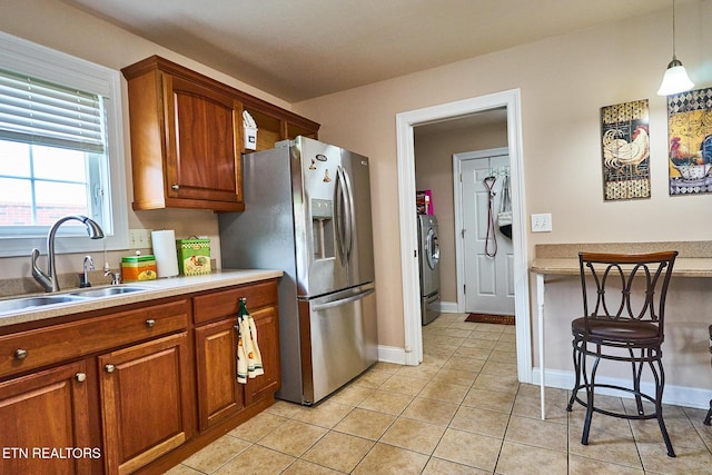 kitchen featuring pendant lighting, washer / clothes dryer, sink, stainless steel fridge, and light tile patterned floors